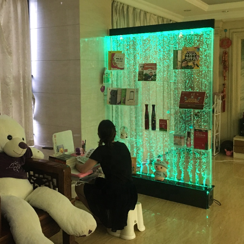 Person sitting in front of a glowing green wall display with various items.